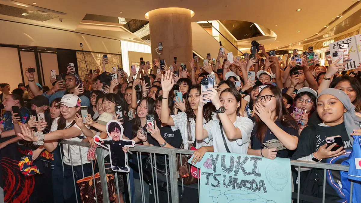 A crowd pressed against the barrier at a mall roadshow in Singapore, phones held up and handmade signs along the front row