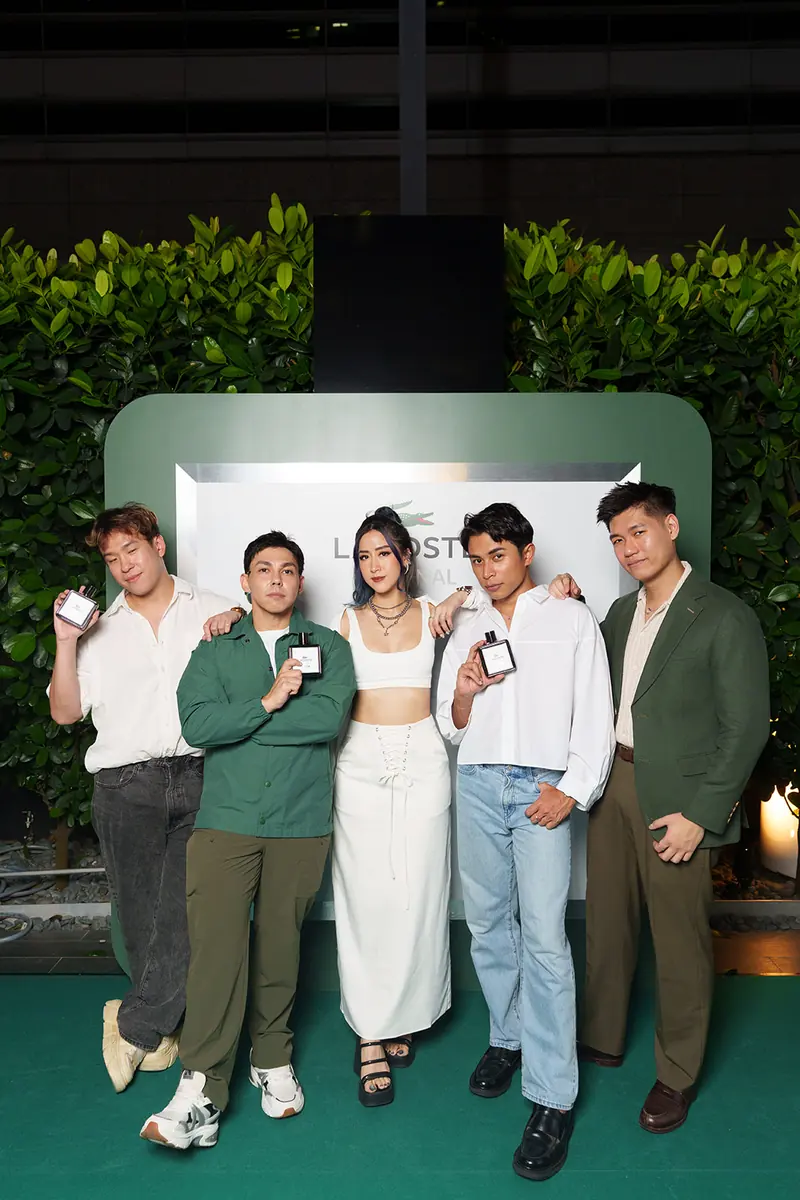 Five guests pose with perfume bottles inside a giant green bottle-shaped photo frame