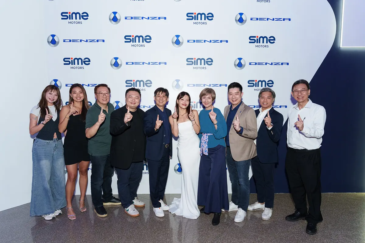 A row of guests stands at a white step-and-repeat wall, each raising one finger and smiling
