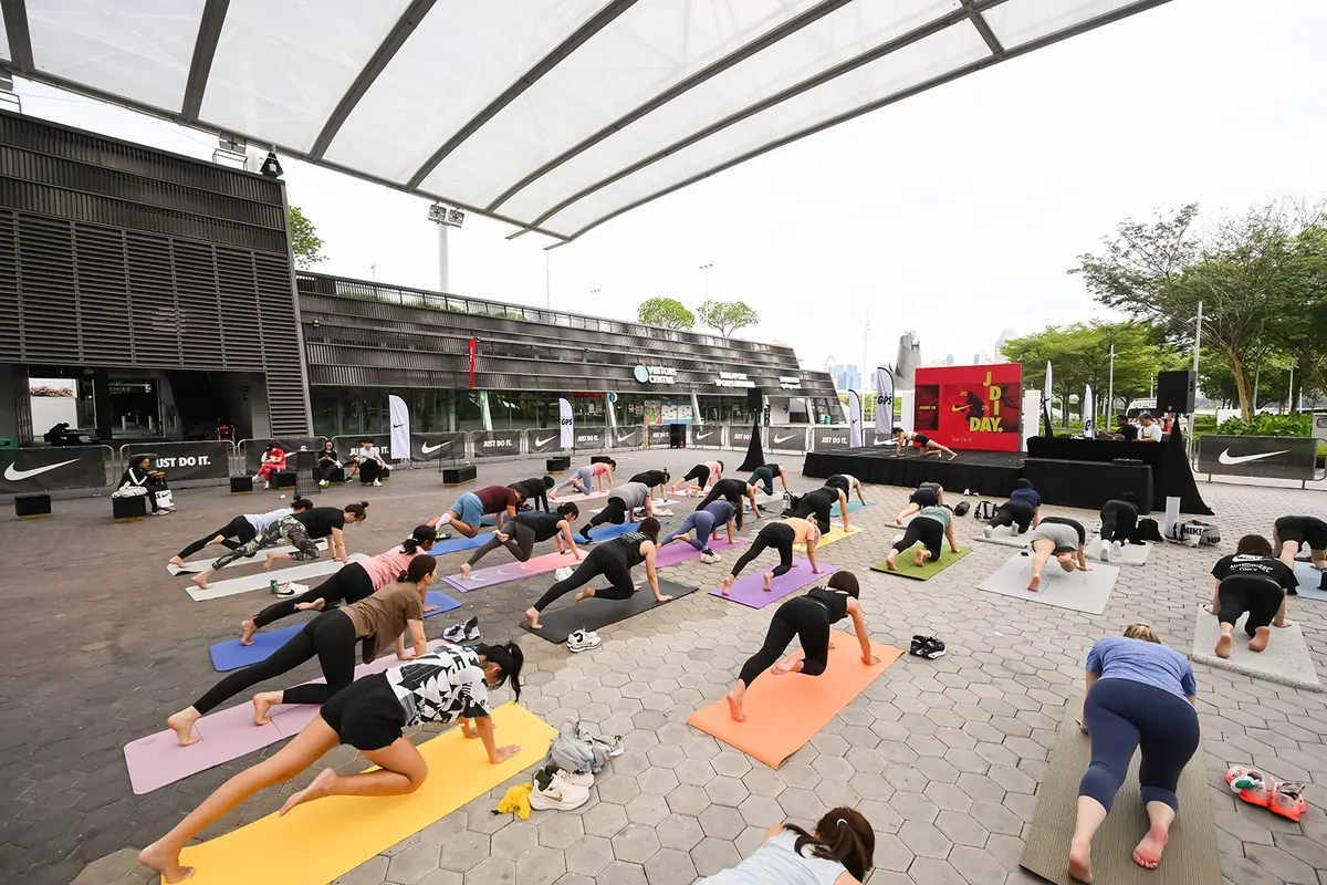 Participants hold planks on mats on an outdoor plaza in front of a small stage with a red backdrop