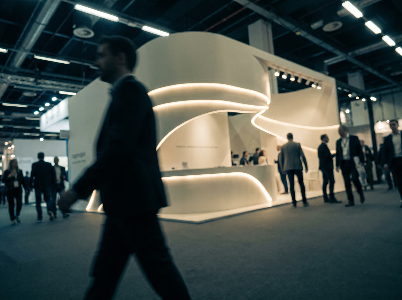 A sculptural concrete exhibition booth with glowing recessed lighting and visitors