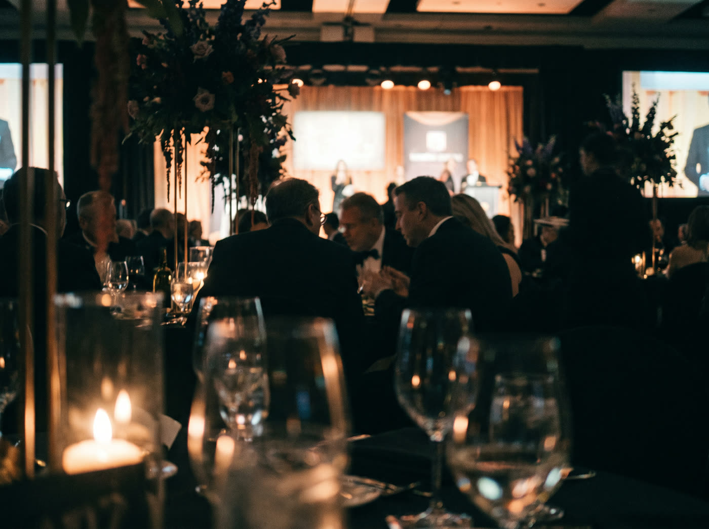 An elegant gala dinner in a grand hall with floral centrepieces and staging